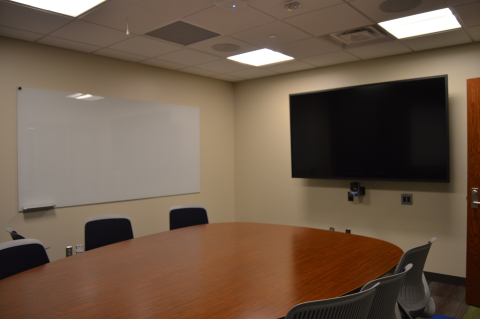 A large table and chairs, a whiteboard, and a large monitor
